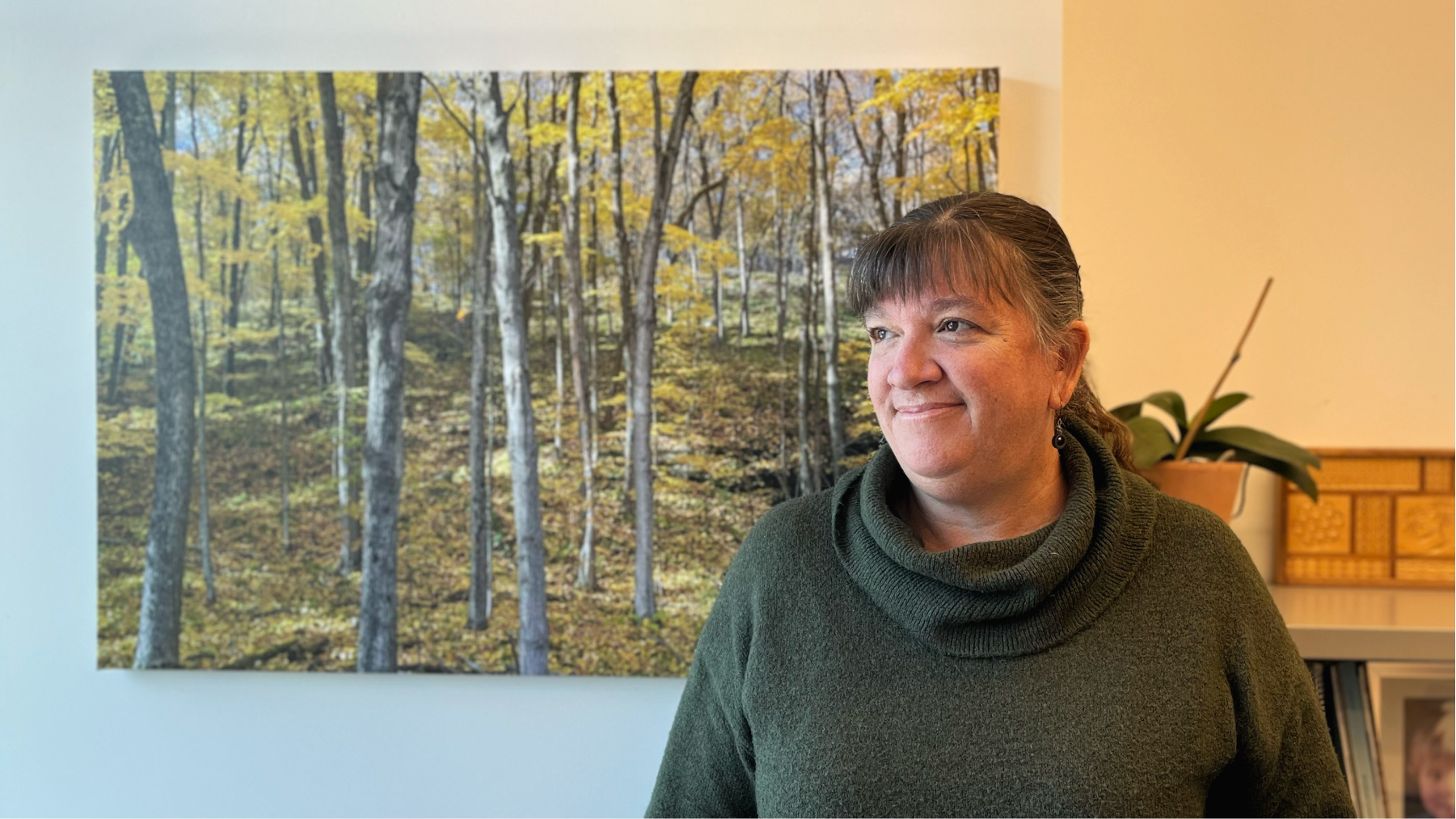 A woman standing in front of a photograph a birch forest in autumn bathed in golden light. 