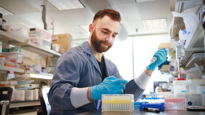 Man with a beard using a pipette in a lab and smiling