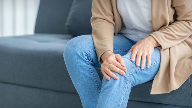 Woman suffering from knee pain sitting sofa in the living room.