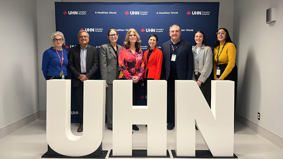 Group image of 8 smiling individuals standing behind 3D letters spelling out UHN.