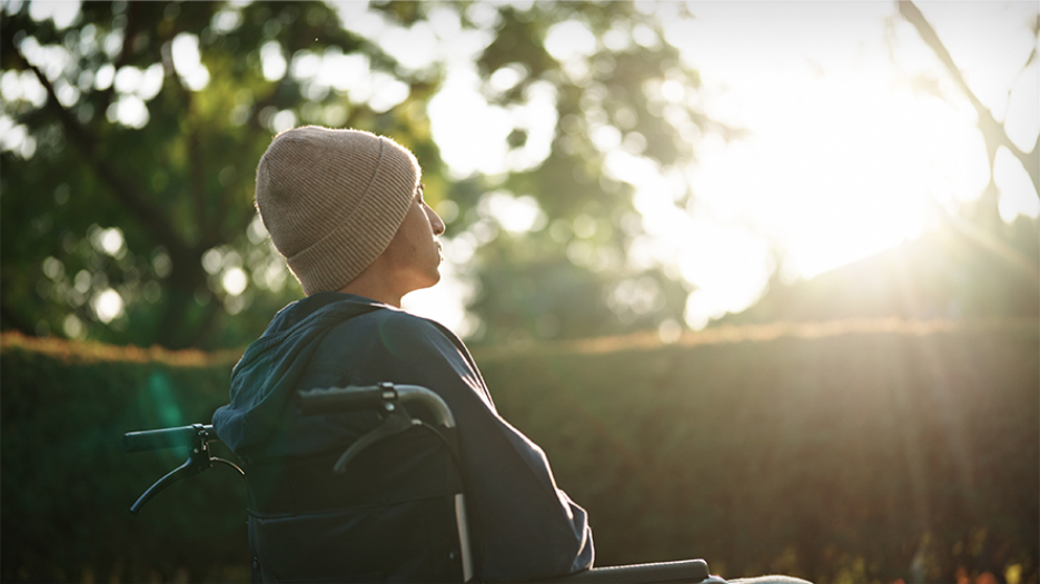 Young male sitting in a wheelchair in an enclosed outdoor space, enjoying in the sun.